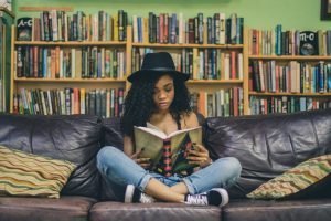 Woman of colour reading on a sofa with bookshelves in background